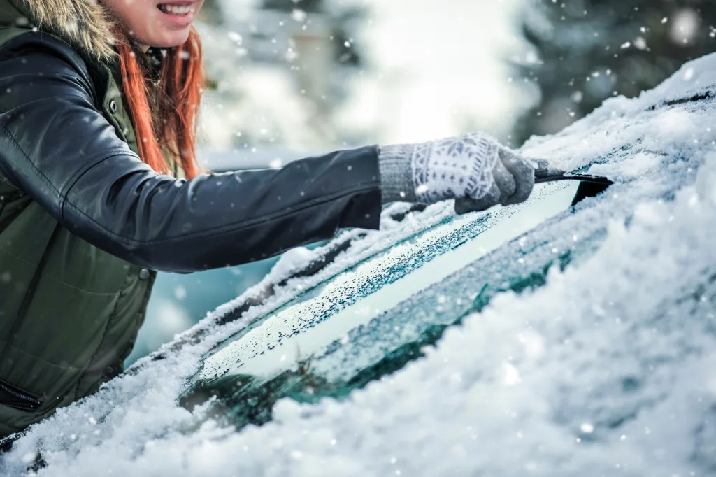 Woman Removing snow from car windshield.