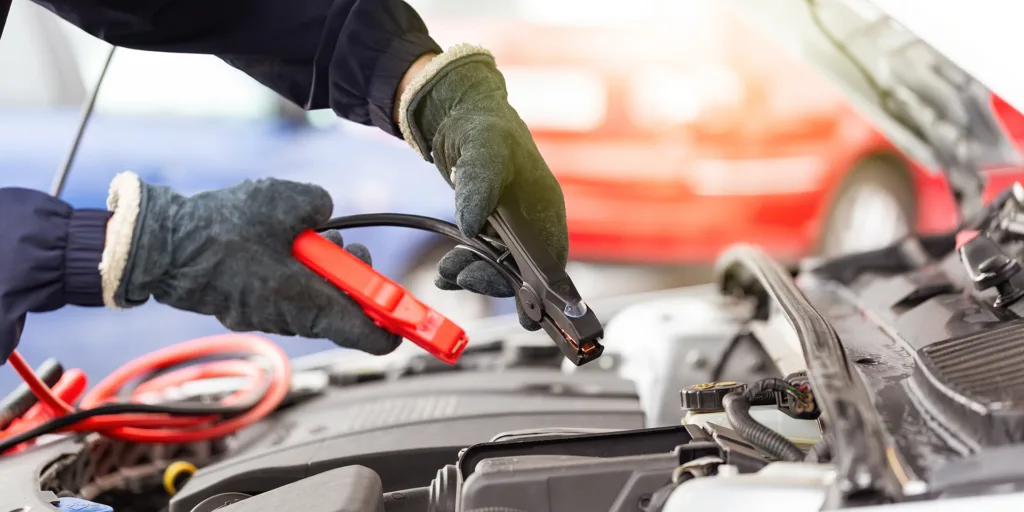 Human hands with jumper cable over the automobile engine in close up